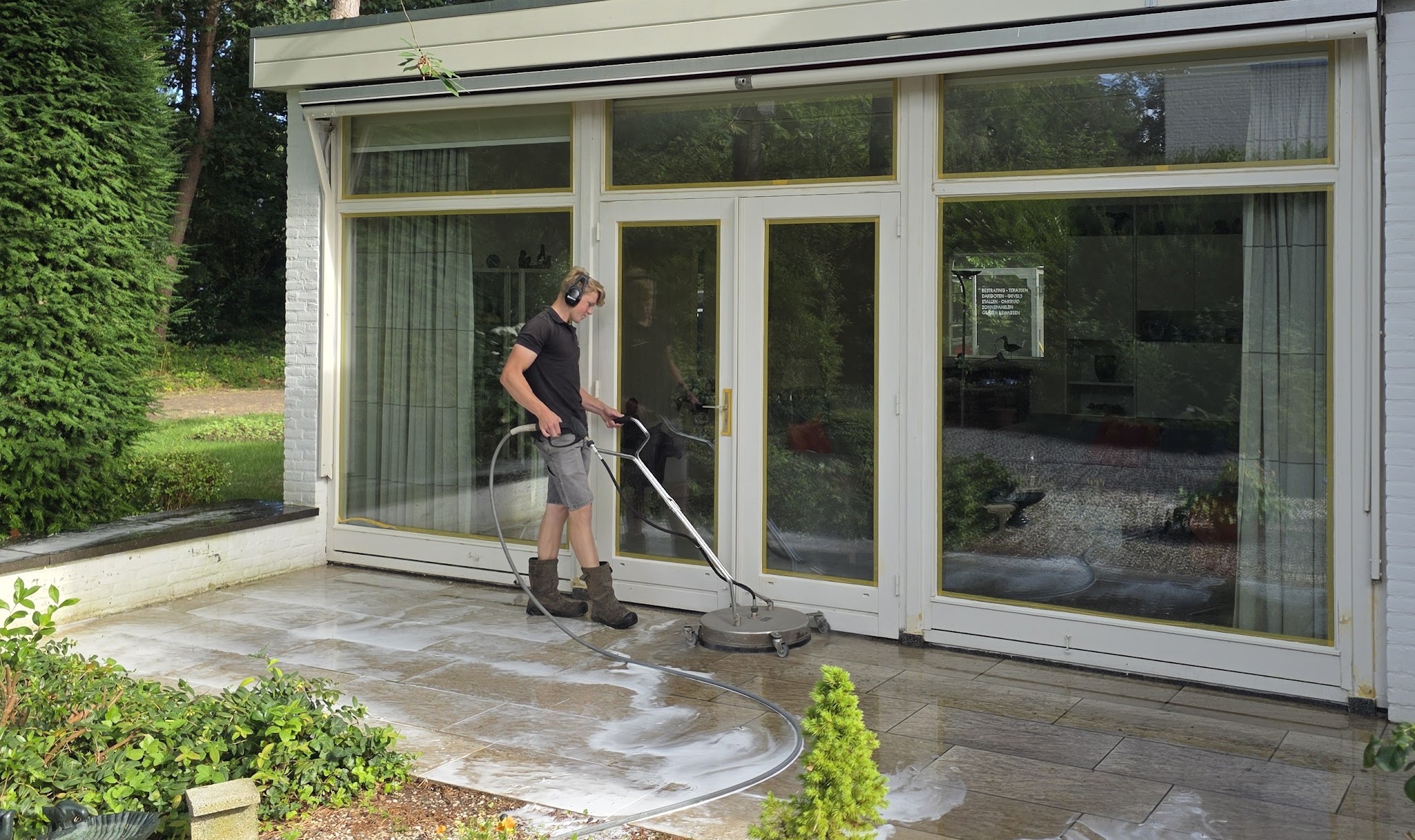 Mike reinigt een terras voor de glazen pui van een woning